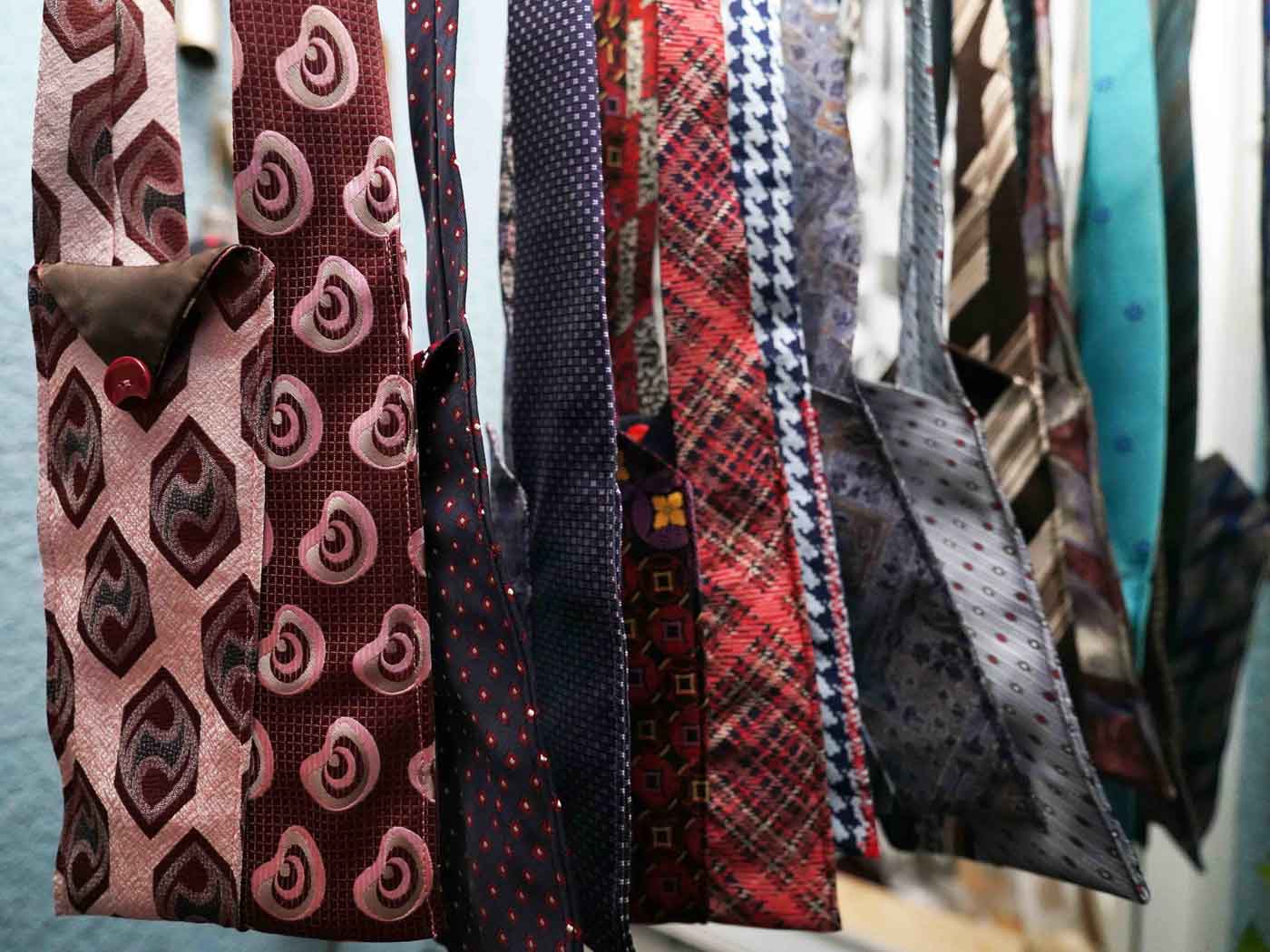 In Else’s Textilwerkstatt genähte Taschen aus bunten Krawatten hängen nebeneinander.
